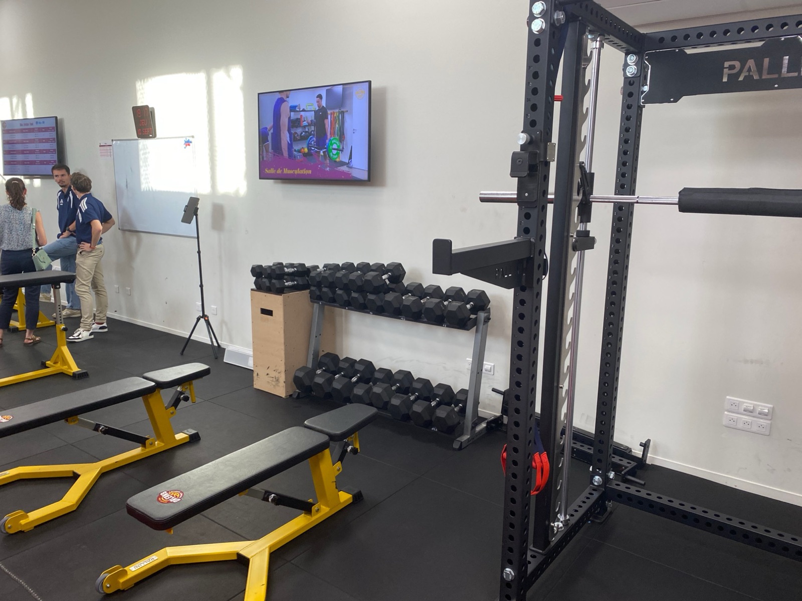 La salle de musculation r&eacute;nov&eacute;e, avec ses bancs jaunes et sa cage &agrave; squat noire